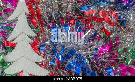 White Christmas tree ornament on multicolored tinsel in background with copy space Stock Photo
