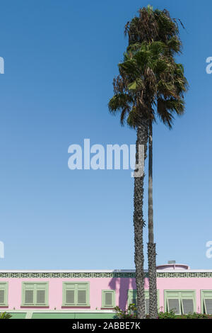 Tall palm trees and the top of a pink tropical style building with light green shutters in Santa Monica, California, USA Stock Photo