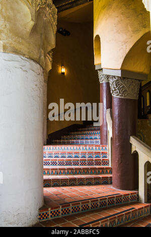 An exterior stairway in  an old Spanish architectural style with beautiful tiles with complex patterns curves through columns in an historic building Stock Photo