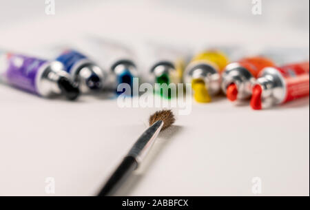 the brush lies in front of the tubes of paint in the order of the colors of the rainbow on the canvas and the paint flows out of them Stock Photo