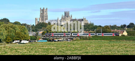 Ely Cathedral beyond train departing Ely Station Cambridgeshire boats on River Great Ouse below railway bridge  East Anglia Fens landscape England UK Stock Photo