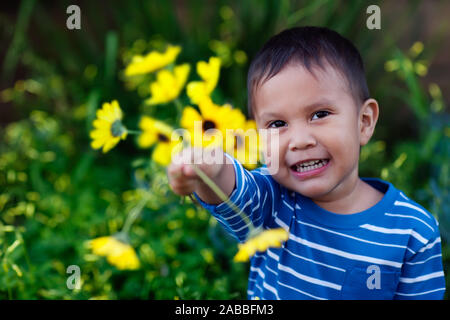 Smiling young son giving an arrangement of yellow flowers he is holding to show affection and love. Stock Photo