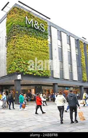 People & shoppers in street scene outside living green wall vertical garden on facade walls of Marks and Spencer store greenery with M&S shop sign UK Stock Photo