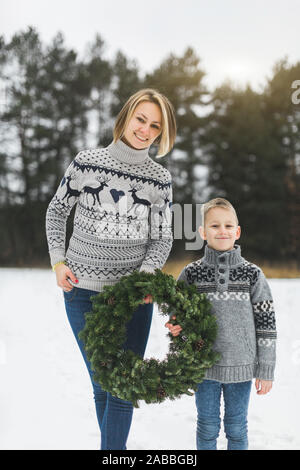 New Year and Christmas Holidays. Caucasian mom with her son holding decorated Christmas wreath in arms while standing outdoors on the background of Stock Photo