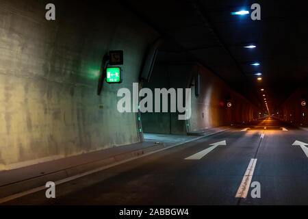 Automobile auto dark car tunnel with white arrows on asphalt showing way direction. Emergency exit sign with many lights. Empty underground vehicle Stock Photo