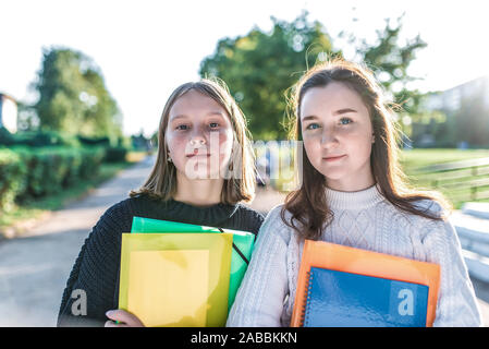 Two schoolgirls girlfriends, in summer in park are standing with notebooks notes. Happy smiles, in warm sweaters autumn day. concept learning at Stock Photo