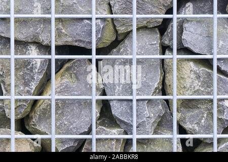 Wall of grey rocks behind a light grey metal grid background Stock Photo