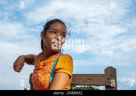 Beautiful young Burmese girl in a bright yellow blouse awaits boarding a water taxi in Kanne village on the Chindwin River in Myanmar (Burma) Stock Photo
