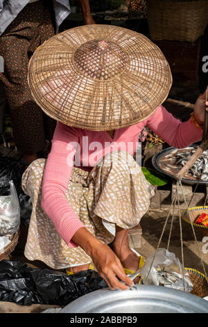 Female fishmonger in traditional conical Asian hat & sarong prepares fish for sale in the Kanne village market by the Chindwin River, Myanmar (Burma) Stock Photo