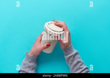 Hands holding reusable coffee cup made from eco friendly bamboo with silicone lid without plastic. Eco friendly zero waste tea mug on blue mint paper. Stock Photo
