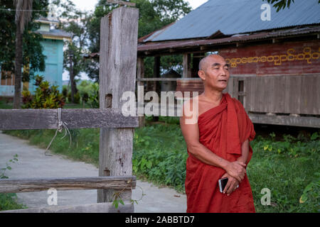 An older Buddhist monk in a scarlet robe stands in front of his monastery in a rural village along the Chindwin River in northwestern Myanmar (Burma) Stock Photo