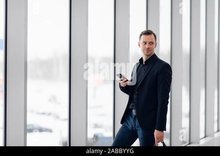 Business man using mobile phone app in airport. Young business professional man texting smartphone walking inside office building or airport terminal Stock Photo