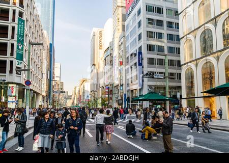 People walking along the Ginza main shopping street, Chuo Dori on a weekend when it is a pedestrian precinct. Fendi fashion store and Mizuho bank. Stock Photo