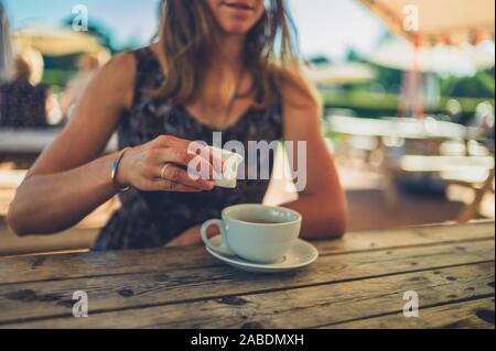 A young woman is drinking coffee at a cafe table outdoors in summer Stock Photo