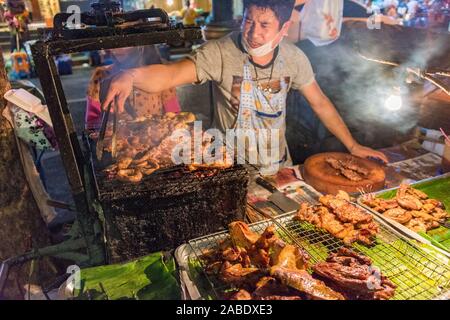 Bangkok, Thailand - December 25, 2015: Night food market scene with man preparing meat on BBQ Stock Photo