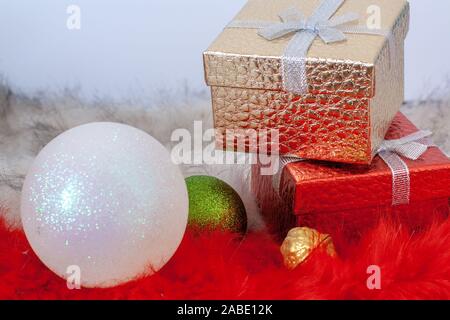 Two gift boxes and two Christmas balls on red and white fur. Holiday card. Selective focus on the boxes. Stock Photo
