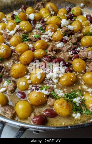 Cooking Greek lamb stew marinated in a white wine salmoriglio sauce with new potatoes kalamata olives feta cheese and mint garnish Stock Photo