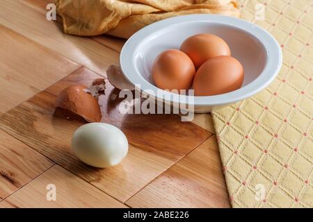 Peeling brown organic hard-boiled farm eggs on wooden kitchen table Stock Photo