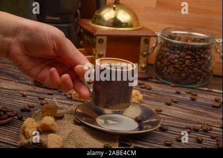 The girl's hand holds a Cup of coffee over a wooden table with brown sugar and coffee beans Stock Photo