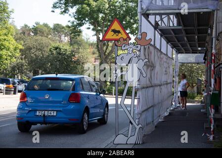 11 July 2019, Sweden, Strömstad: A car drives past a cardboard moose in Strömstad. He's holding onto a warning sign for 'Beware Moose.' Photo: Stephan Schulz/dpa-Zentralbild/ZB Stock Photo