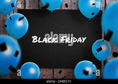 Black Friday text on black paper surrounded with blue ballons and black confetty. Stock Photo