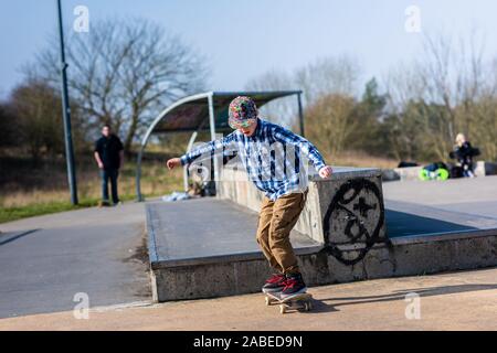 A cute little boy with Asperger syndrome, ADHD, Autism riding around at the skatepark listening to music and practicing tricks, down steps, Ollie etc Stock Photo