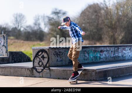 A cute little boy with Asperger syndrome, ADHD, Autism riding around at the skatepark listening to music and practicing tricks, down steps, Ollie etc Stock Photo