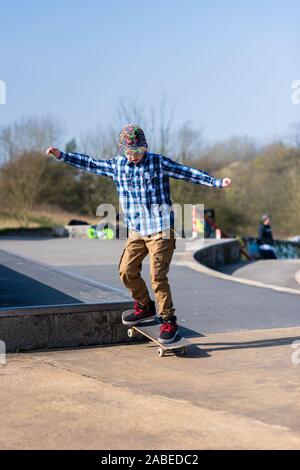 A cute little boy with Asperger syndrome, ADHD, Autism riding around at the skatepark listening to music and practicing tricks, down steps, Ollie etc Stock Photo