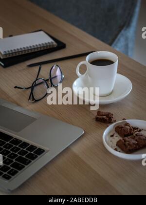 Freelancer desktop with laptop, notes, glasses, coffee cup and cookies Stock Photo