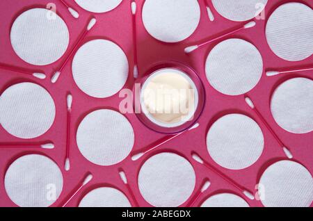 Hygiene products: white round cotton pads and plastic sticks for cleaning the ears lie on a pink background next to face cream Stock Photo