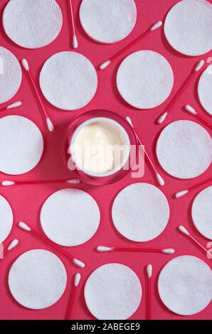 Hygiene products: white round cotton pads and plastic sticks for cleaning the ears lie on a pink background next to face cream Stock Photo