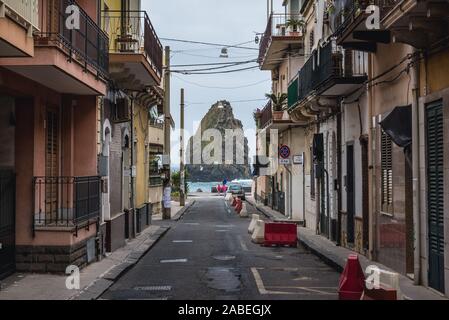 Street in Aci Trezza town, a frazione of Aci Castello comune near Catania on Sicily Island in Italy - Cyclopean Isles sea stack on background Stock Photo