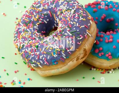 round baked donut with colored sugar sprinkles and with blue sugar icing on a green background, close up Stock Photo