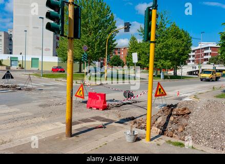 Warning signs for work in progress on road under construction.  fiber optic cables buried in a micro trench with concrete colored red by a worker Stock Photo