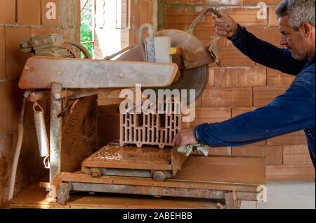 Worker using an angle grinder or circular saw cutting bricks in construction site Stock Photo