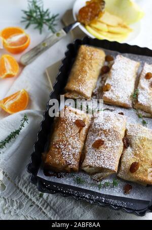 Top view of homemade phyllo dough rolls with apples and orange marmalade. White background with sultanas. Stock Photo