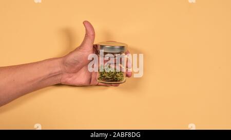 a glass bank with fresh marijuana buds in the hands of a man. Flat lay, top view. Concept of herbal and alternative medicine Stock Photo
