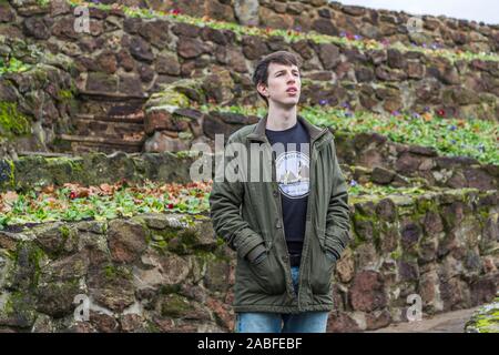 A handsome young man in his late teens or early twenties stands outdoors and looks into the distance with a worried or concerned expression. Stock Photo