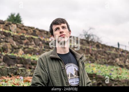 A handsome young man in his late teens or early twenties stands outdoors and looks into the distance with a hopeful and optimistic expression. Stock Photo