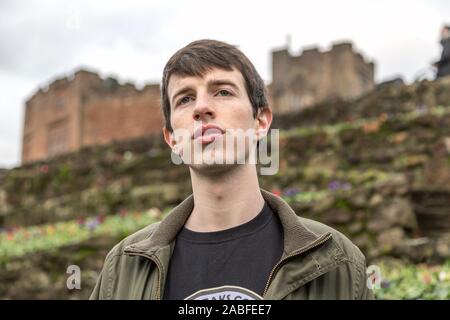 A handsome young man in his late teens or early twenties stands outdoors and looks into the distance with a hopeful and pensive expression. Stock Photo