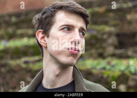 A confident handsome young man in his late teens or early twenties stands outdoors and looks to the side. Stock Photo