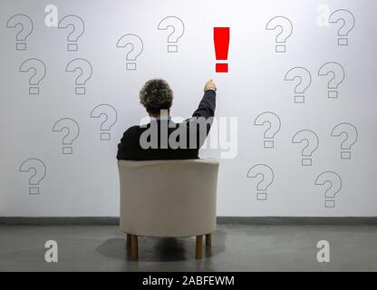 a man points to an exclamation point among many question marks. concept of idea, certainty, solution Stock Photo