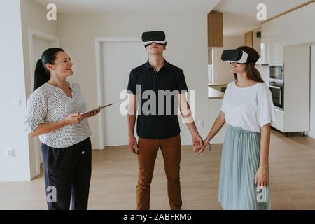 Estate agent with young couple wearing VR headsets in new apartment Stock Photo