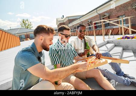male friends eating pizza with beer on rooftop Stock Photo