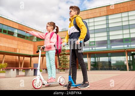 happy school children with backpacks and scooters Stock Photo