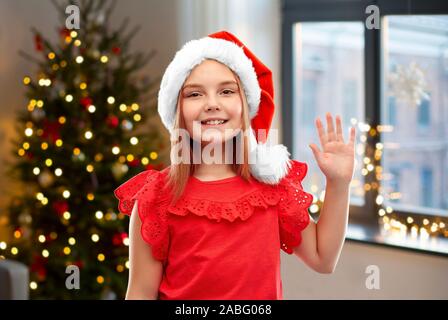 happy girl in santa helper hat waving hand at home Stock Photo