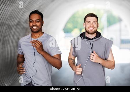 male friends with earphones running outdoors Stock Photo