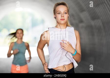 women or female friends with earphones running Stock Photo