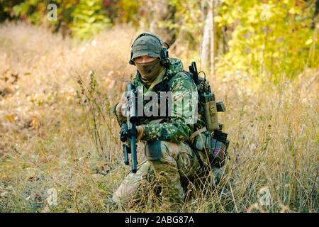 Airsoft man in uniform with sniper rifle, lurking in grass. Stock Photo