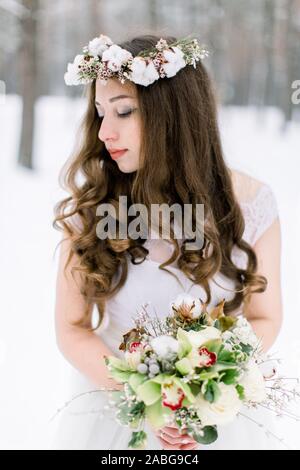 Portrait of a beautiful young woman, bride, in a winter forest. Bride with wreath on the head, made from cotton, holding winter bouquet Stock Photo